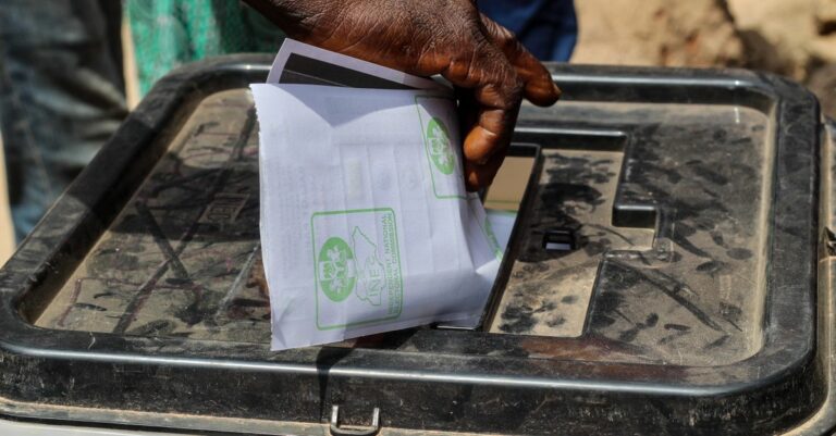Une main glisse un bulletin de vote dans une urne transparente