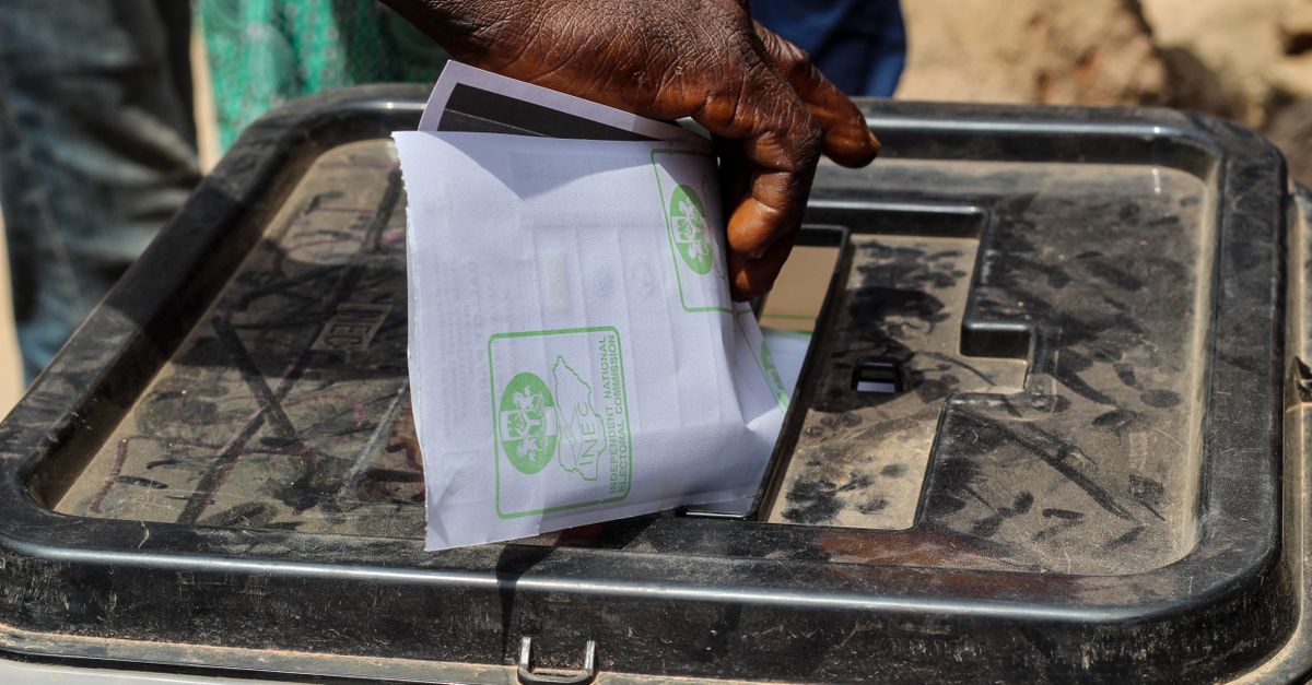 Une main glisse un bulletin de vote dans une urne transparente